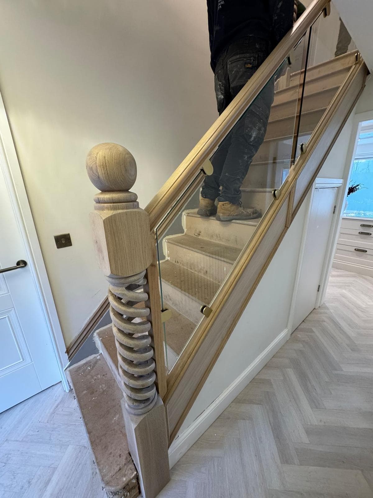 Barley-twist oak newel post with a turned ball-cap finial beside a herringbone hallway floor