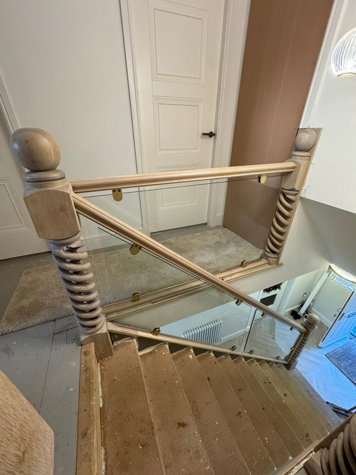 Top-down view of oak barley-twist newel posts and a glass balustrade around an open stairwell