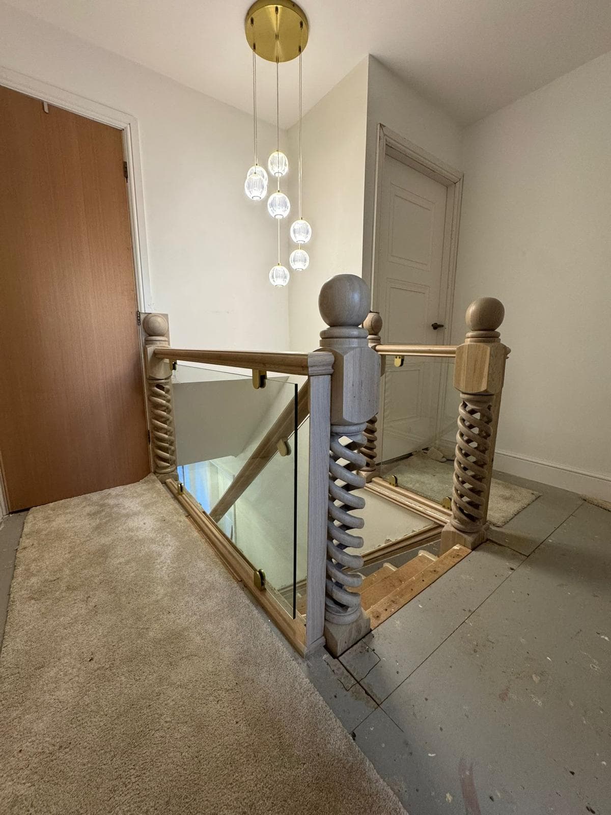 Oak glass balustrade and barley-twist newel posts on a landing beneath a cluster of pendant lights